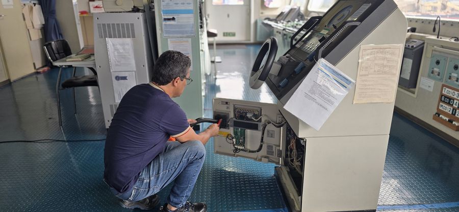 Técnico da MCO agachado no passadiço de um navio, com o console aberto para reparo